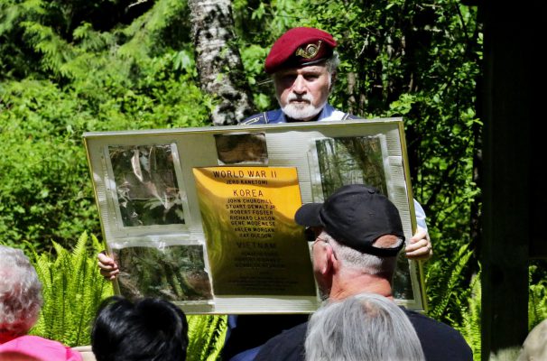 Bernie Moskowitz, class of 1957 and president of the Cleveland High Alumni Association, shows a display of names listed on brass along with photos of the forest to people gathered for the annual memorial to the fallen. (Alan Berner/The Seattle Times)