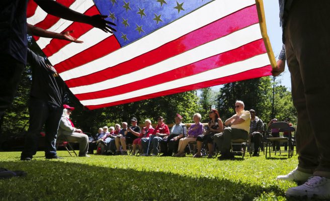 With the stars and stripes held by Cleveland High seniors, alumni and family gather Friday at the annual memorial for their fallen in war and to dedicate the new granite monument honoring them at the Cleveland High School Memorial Forest. (Alan Berner/The Seattle Times)
